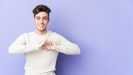 Young caucasian man isolated on purple background smiling and showing a heart shape with hands.