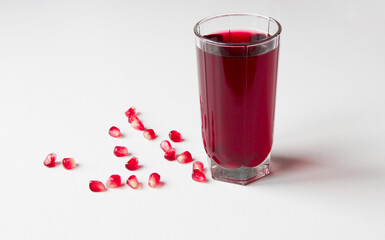 A glass of pomegranate juice. Next to a glass of bright and ripe pomegranate seeds on a white background.