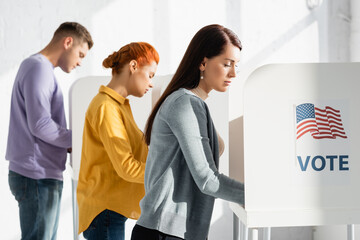 voters in polling cabins with american flag and vote lettering on blurred background