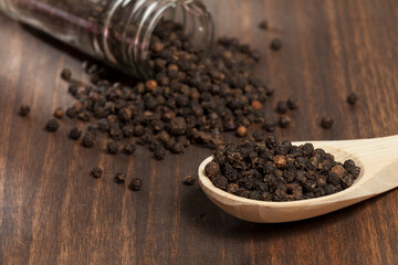 Piper nigrum - black peppercorns; photo on dark wooden background.