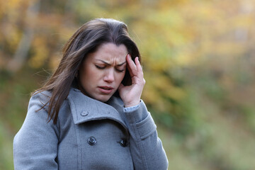 Stressed woman suffering migraine in a park in winter
