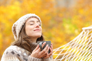 Woman breaths fresh air holding coffee cup in autumn