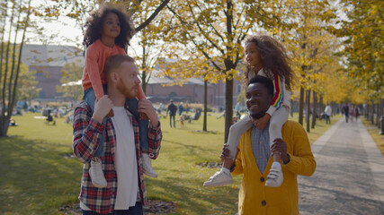 Portrait of diverse gay parents and little daughters walking in fall park