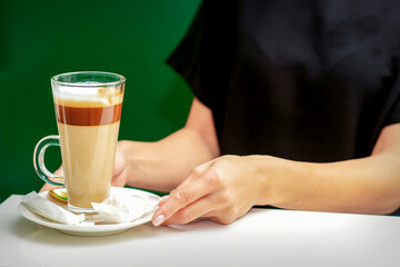 Close up of female waiter gives cup of coffee latte with candy in plate on the table