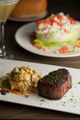 Surf ‘n Turf, lobster tail and steak entree. Filet mignon topped with chanterelle mushrooms & Maine lobster tail topped w/ drawn butter served on white dinner plate. Classic steakhouse menu favorite.