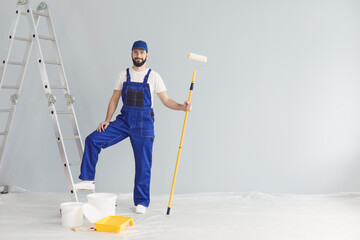 Smiling worker painter standing with paint roller in apartment for repairs and looking at camera