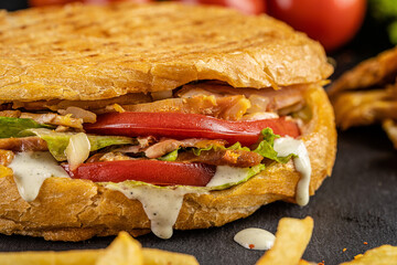 Turkish kebab in a fried bun with chicken, tomatoes, salad and cheese on a black background.