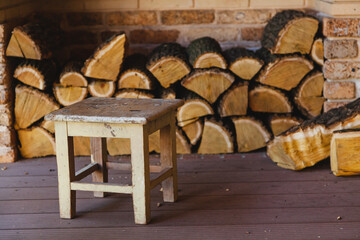 Fototapeta na wymiar Wooden stool stands in front of stacked firewood