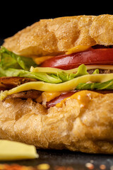 Turkish kebab in a fried bun with chicken, tomatoes, salad and cheese on a black background.