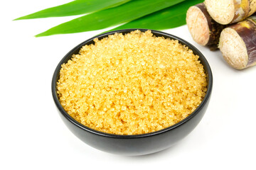 Sugar from sugarcane in black bowl, green leaf and pile of sugarcane isolated on white background.