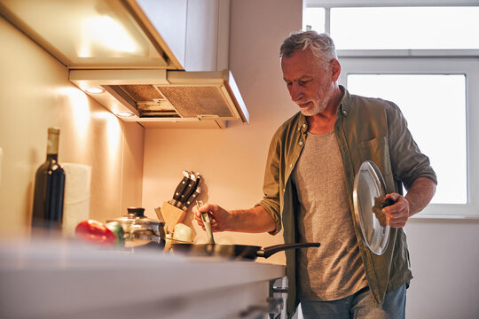 Senior gentleman lifting the lid off frying pan on cooker