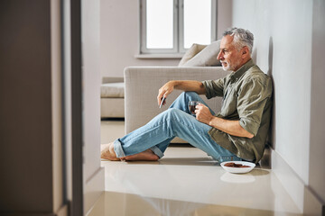 Grey-haired gentleman having tea with cookies on the floor