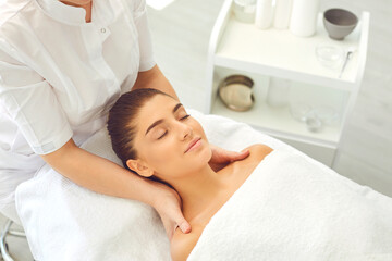 Good looking female client getting face and neck massage lying on bed in beauty parlor