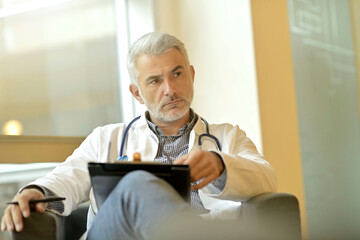 Fototapeta premium Mature doctor writing report with anxious thought