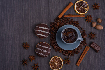 A cup of espresso is decorated with anise stars, cinnamon, sweets, dried lemons, acorns, peanuts in a beautiful dish.
