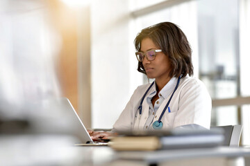 Woman doctor working in office with laptop computer - 389644535