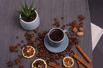 A cup of espresso is decorated with anise stars, cinnamon, sweets, dried lemons, acorns, peanuts in a beautiful dish.
