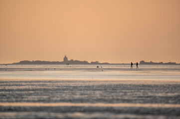 Menschen im Watt von Cuxhaven im Sonnenuntergang mit Insel Neuwerk im Hintergrund