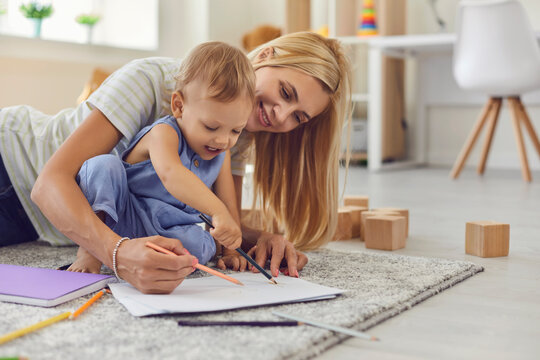 Happy smiling woman mother and baby kid sitting on floor carpet and drawing on paper together
