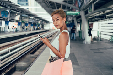 Beautiful woman using mobile phone and holding shopping bags at train station