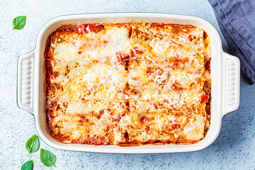Traditional cannelloni with meat, tomato sauce and cheese in a dish, gray background, top view. Italian cuisine concept.