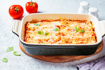 Traditional cannelloni with meat, tomato sauce and cheese in a dish, gray background. Italian cuisine concept.