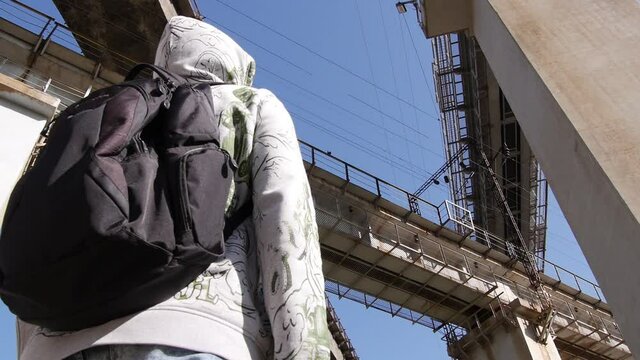 A man with a black backpack looks up at 3 high viaducts. Railway bridges.