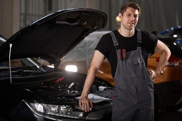 portrait of confident caucasian mechanic in uniform posing at camera in auto service, young male likes his work connected with repair of cars