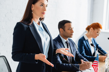 Confident female politician gesturing and looking away in boardroom on blurred background