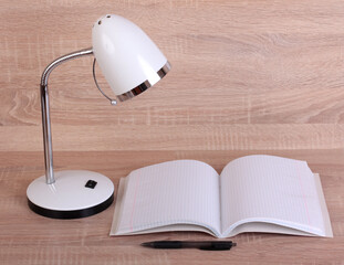 White metal table lamp and notebook on wooden board