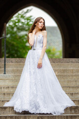 Naklejka premium Beautiful girl wearing white wedding dress posing alone on the chapel stairs