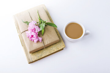 Obraz na płótnie Canvas Romantic vintage still life with old book, cup of tea or coffee, pretty gift box wrapped with craft paper and decorated with pink flower on white background.
