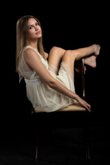 piękna seksowna modelka kobieta dziewczyna w studiu w białej sukience na czarnym tle na krześle