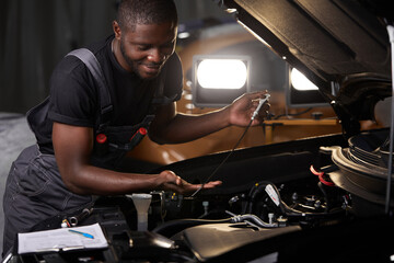 professional car mechanic is examining engine under the hood at auto repair shop, make notes, checking notes in notebook