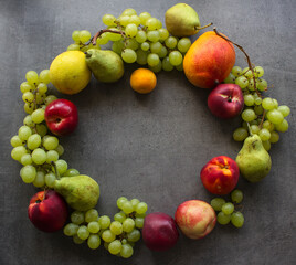 Summer fruit composition. Colorful grapes, nectarines, mango and pears wreath top view photo. Dark grey textured background with copy space. 