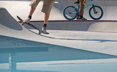 Young active men riding skateboard and BMX bike in concrete skatepark