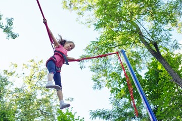 Child girl having fun jumping on trampoline with elastic ropes