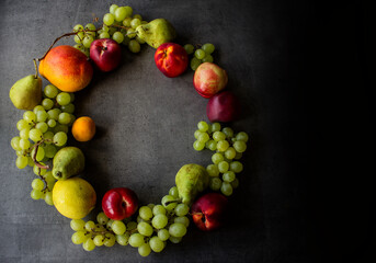 Summer fruit composition. Colorful grapes, nectarines, mango and pears wreath top view photo. Dark grey textured background with copy space. 