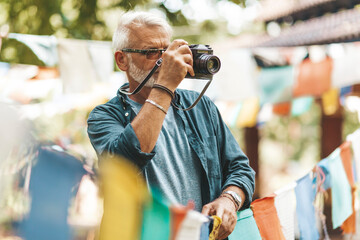 A European senior tourist photographs prayer flags in Nepal.