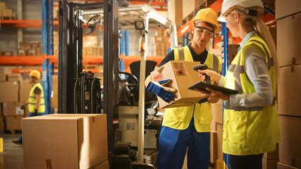 In Warehouse Manager Uses Digital Tablet and Scans Cardboard Boxes for Inventory, Talks with Forklift Driver about Package Delivery. Workers in Global Distribution Center with Shelves with Goods  - obrazy, fototapety, plakaty