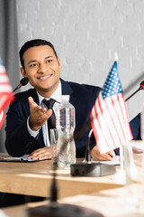 Smiling indian politician pointing with hand, while looking away, sitting near colleague on blurred foreground