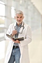 Portrait of confident doctor with grey hair standing in hospital hallway