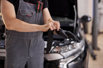 close-up photo of young auto service worker wearing black gloves, he is going to repair a car, opened hood of auto in the background