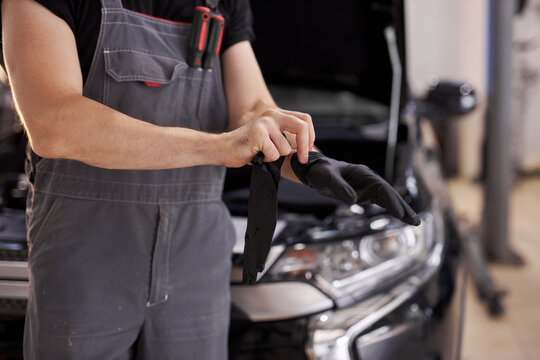 close-up photo of young auto service worker wearing black gloves, he is going to repair a car, opened hood of auto in the background