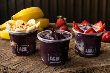 Mix of Delicious Brazilian Açaí Cream, in a plastic Cup With a variety of Toppings, in a rustic wooden background. Summer acai smoothie