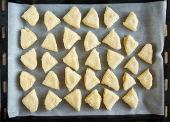 The raw curd triangular cookies are on a baking sheet. View from above