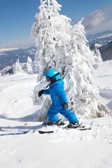 Fototapeta na wymiar toddler boy in helmet, goggles and blue overalls skiing in beautiful snowy mountains. Winter active entertainment for children. Skiing lesson at an alpine school. Cold, sunny, beautiful