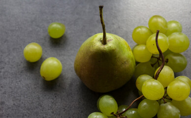 Still life with green pears and grapes on dark grey textured background. Summer fruits close up photo. 