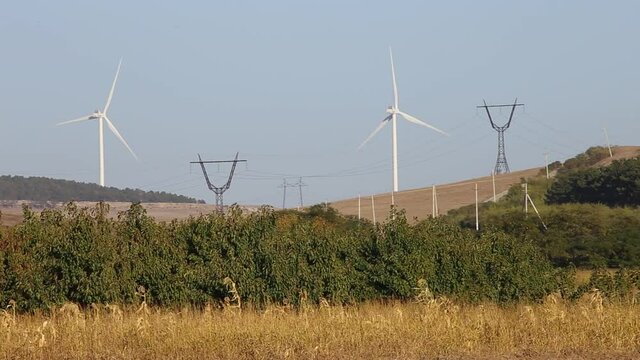 Rotating blades of wind turbines against a blue sky surrounded by fields