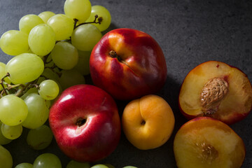 Beautiful fresh fruits on dark grey table: green grapes, nectarines, apricot. Summer fruits top view. 